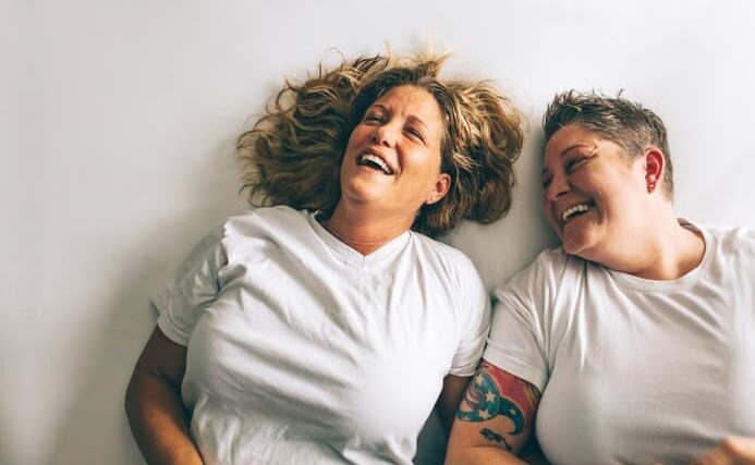 Lesbian couple joyfully laughing while laying in bed.